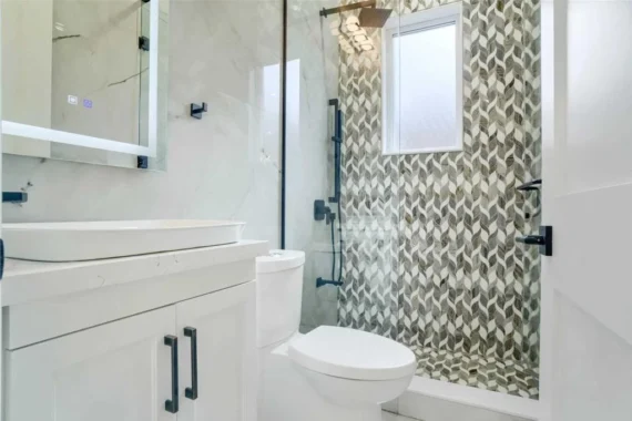 Modern bathroom renovation with glass shower enclosure, white vanity cabinet, vessel sink, and patterned shower wall tiles.
