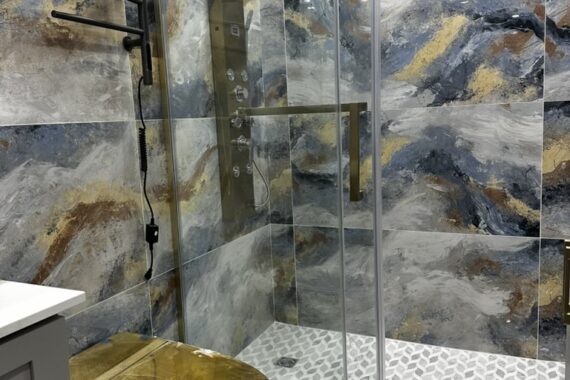 Luxury bathroom with glass shower enclosure, patterned wall tiles, gold shower fixtures, sliding glass door, and textured tile flooring.