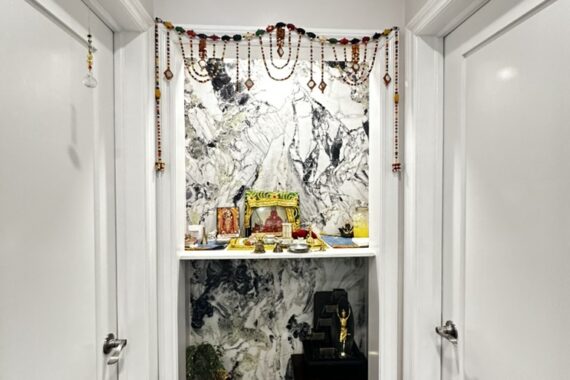 Hallway prayer niche with marble-look wall finish, built-in shelves, decorative hanging garlands, and wooden flooring.