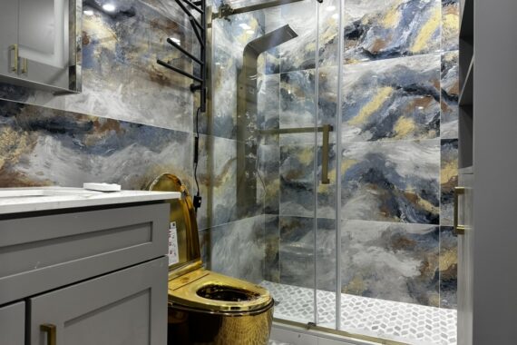 Luxury bathroom with glass shower enclosure, patterned wall tiles, gold shower fixtures, sliding glass door, and textured tile flooring.