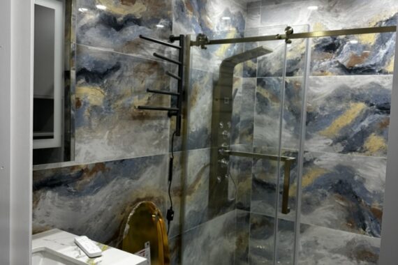 Luxury bathroom with glass shower enclosure, patterned wall tiles, gold shower fixtures, sliding glass door, and textured tile flooring.