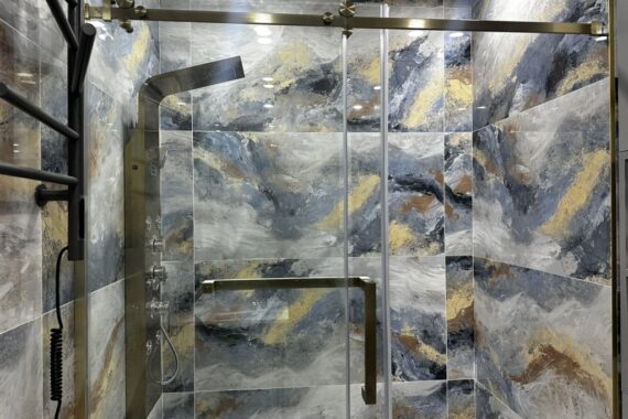 Walk-in shower with sliding glass door, patterned wall tiles, gold shower fixtures, rainfall shower panel, and recessed ceiling lighting.