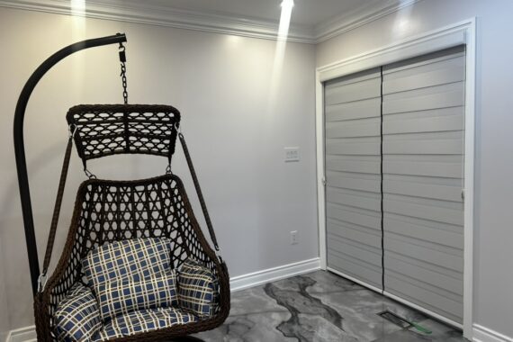 Modern interior room with tiled flooring, light-colored walls, window blinds, and a hanging swing chair with cushions.