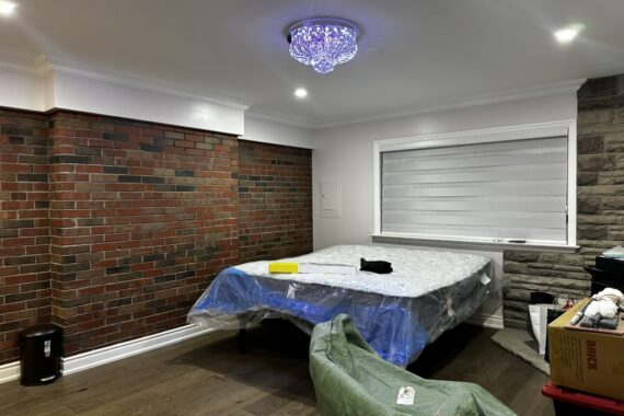 Bedroom interior with exposed brick accent wall, stone feature wall, hardwood flooring, recessed ceiling lights, and modern chandelier.
