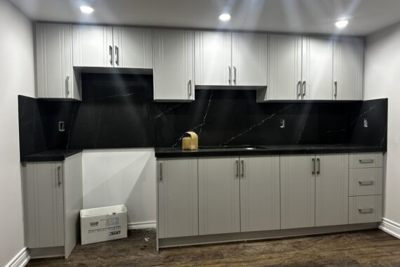 Modern kitchen renovation with white shaker cabinets, black stone backsplash, matching black countertops, and recessed ceiling lighting.