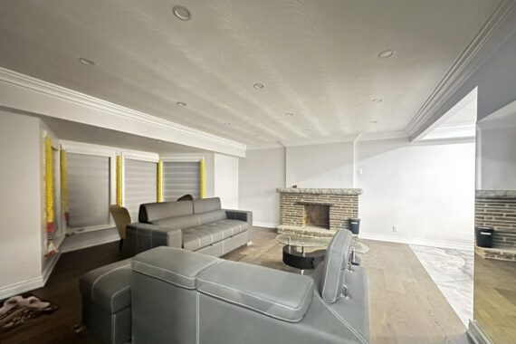 Finished basement living room with sectional sofas, hardwood flooring, recessed ceiling lights, brick fireplace, and large open layout.