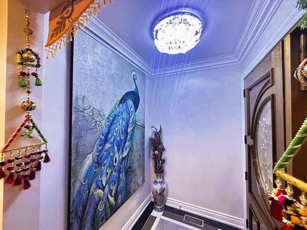 Entryway interior with decorative peacock wall art, modern ceiling chandelier, crown molding, and custom front door.