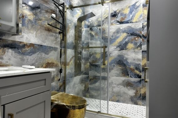 Luxury bathroom with glass shower enclosure, patterned wall tiles, gold shower fixtures, sliding glass door, and textured tile flooring.