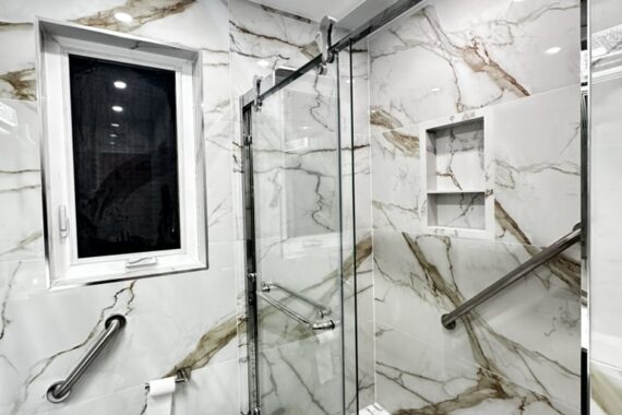 Modern bathroom renovation with marble-look wall tiles, glass shower enclosure, hexagon shower floor tiles, floating vanity, and black fixtures