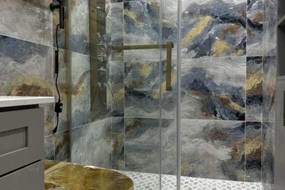 Luxury bathroom with glass shower enclosure, patterned wall tiles, gold shower fixtures, sliding glass door, and textured tile flooring.