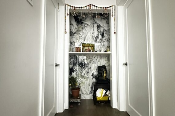 Renovated hallway with wooden flooring, white interior doors, and a custom prayer niche featuring marble-look wall panels and built-in shelving.