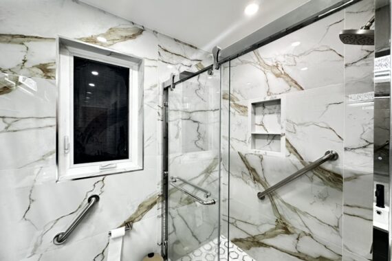 Bathroom with marble-look wall tiles, glass shower enclosure, built-in shower niche, grab bars, hexagon tile shower floor, and recessed lighting.