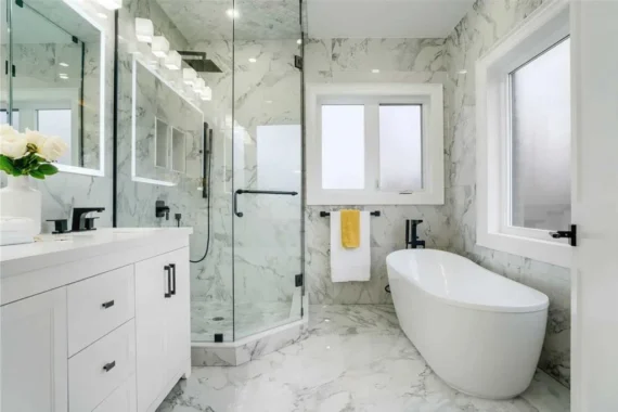Luxury bathroom renovation with freestanding bathtub, marble tile walls, and frameless glass shower enclosure.