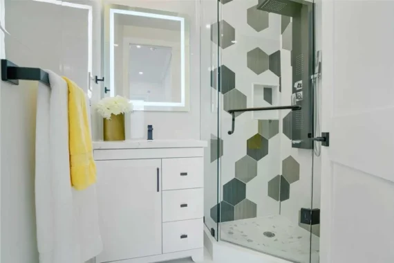 Modern bathroom renovation with hexagon tile shower wall, frameless glass shower enclosure, and white vanity with LED mirror.