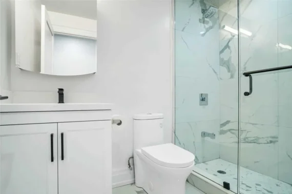 Modern bathroom renovation with marble tile shower, frameless glass enclosure, white vanity cabinet, and black faucet.