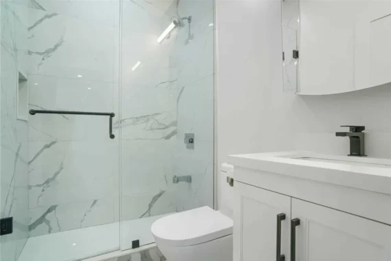 Modern bathroom renovation with marble wall tiles, frameless glass shower enclosure, and white vanity with black faucet.